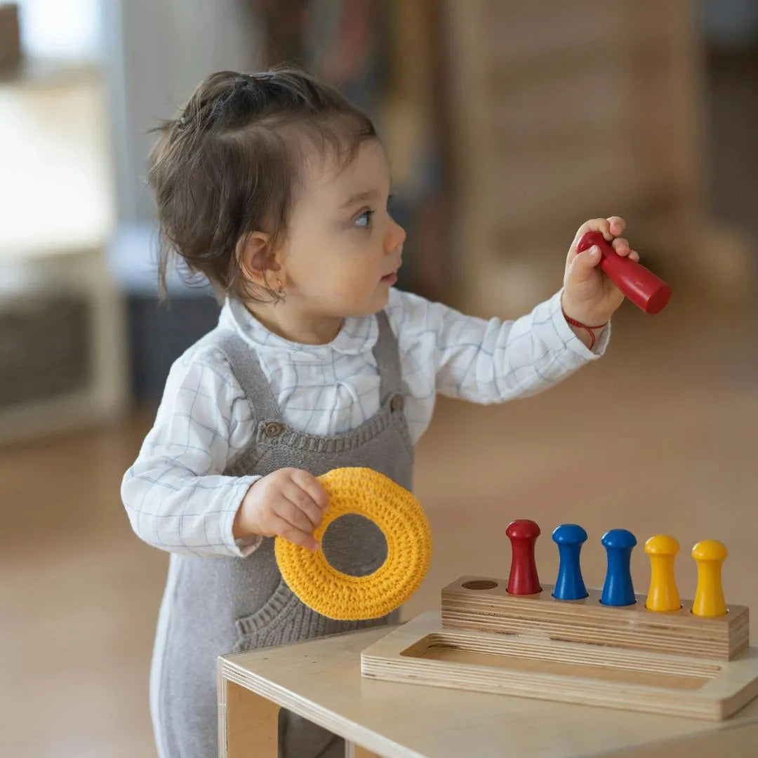 little girl dressed with a with shirt and grey pants, playing with a montessori toy or educational toy witch consist in put little pins in the right hole