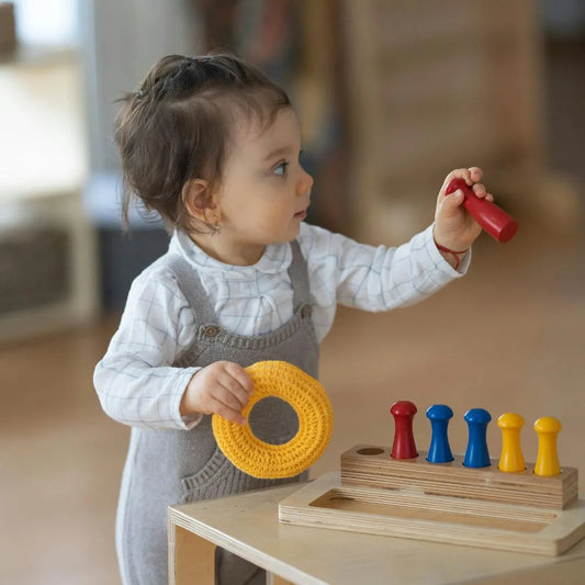 little girl dressed with a with shirt and grey pants, playing with a montessori toy or educational toy witch consist in put little pins in the right hole